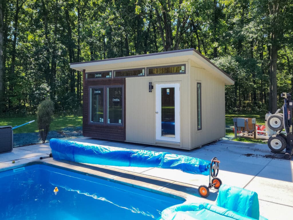 Tan colored modern studio pool house beside a pool.